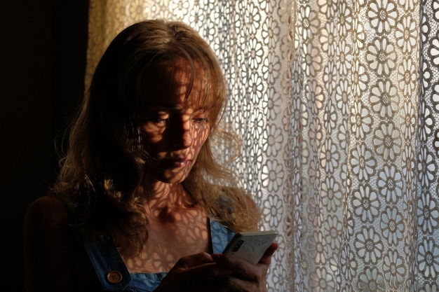 Photo belle jeune fille regarde le téléphone le jeu de lumière et d'ombre sur le corps. image d'ombre légère.