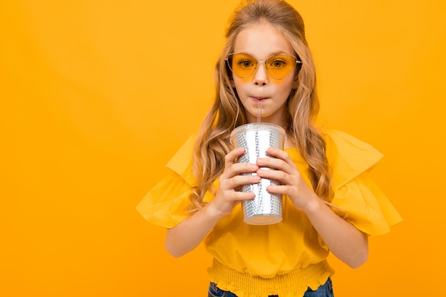 Belle jeune fille en robe jaune boit du jus sur un fond jaune