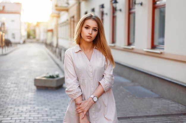 Belle jeune fille en robe rose marchant dans la ville au coucher du soleil