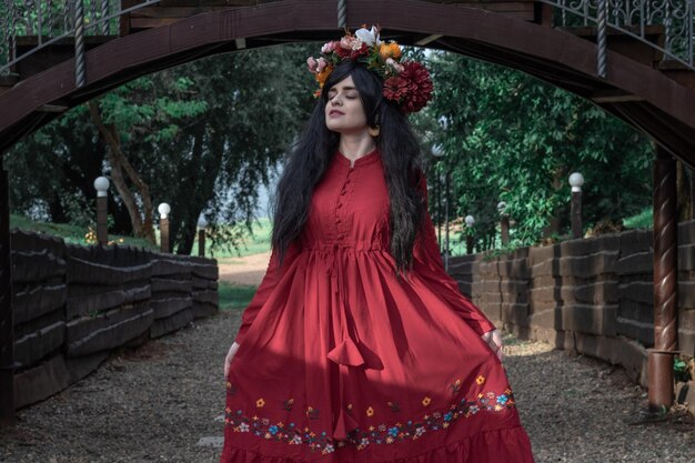 Belle jeune fille en robe rouge à manches longues et une couronne danse sous le pont dans le parc