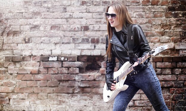 Belle jeune fille rocker avec guitare électrique. Une fille musicienne de rock dans une veste en cuir avec une guitare chante. Un soliste d'un groupe de rock joue de la guitare et crie dans le micro.
