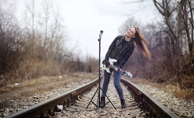 Belle jeune fille rocker avec guitare électrique. Une fille musicienne de rock dans une veste en cuir avec une guitare chante. Un soliste de groupe de rock joue de la guitare et crie dans le microphone.