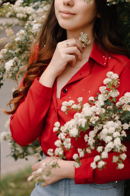 Belle jeune fille rousse dans un chemisier rouge au printemps près des buissons fleuris