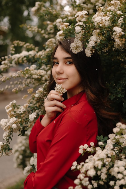 Belle jeune fille rousse dans un chemisier rouge au printemps près des buissons fleuris