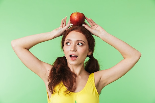 belle jeune fille rousse émotionnelle posant isolée sur fond de mur vert avec pomme.