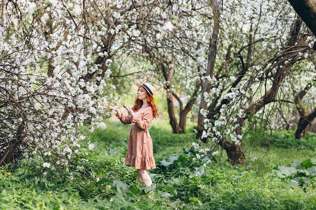 Belle jeune fille rousse se promène dans un verger de pommiers en fleurs au printemps