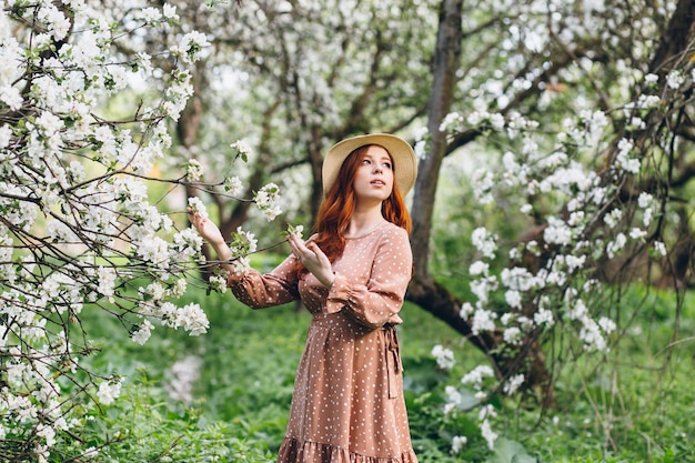 Belle jeune fille rousse se promène dans un verger de pommiers en fleurs au printemps