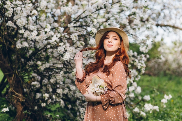 Belle jeune fille rousse se promène dans un verger de pommiers en fleurs au printemps