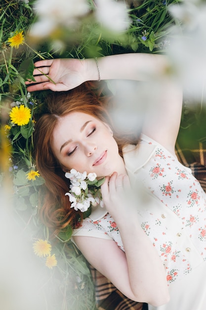 Belle jeune fille rousse se promène dans un verger de pommiers en fleurs au printemps