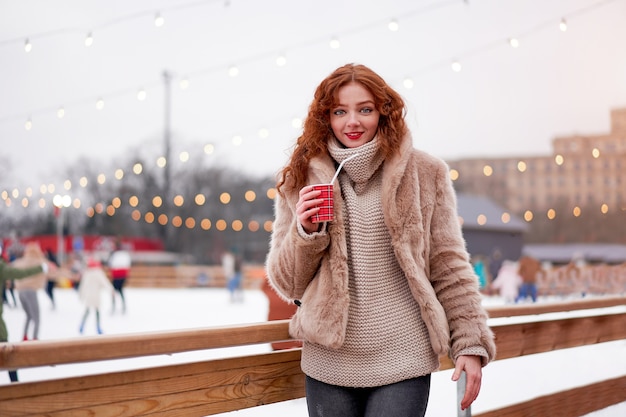 Belle jeune fille rousse taches de rousseur sur la patinoire. Jolie femme portrait de cheveux bouclés marchant sur la foire du nouvel an