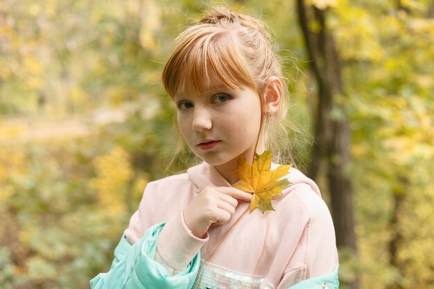 Belle jeune fille s'amusant avec des feuilles dans un parc en automne