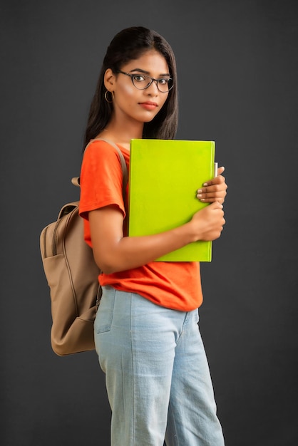 Belle jeune fille avec un sac à dos debout et tenant un cahier posant sur un fond gris