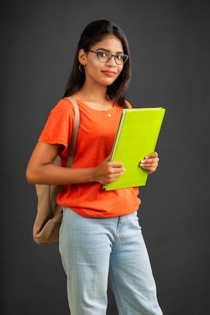 Belle jeune fille avec un sac à dos debout et tenant un cahier posant sur un fond gris