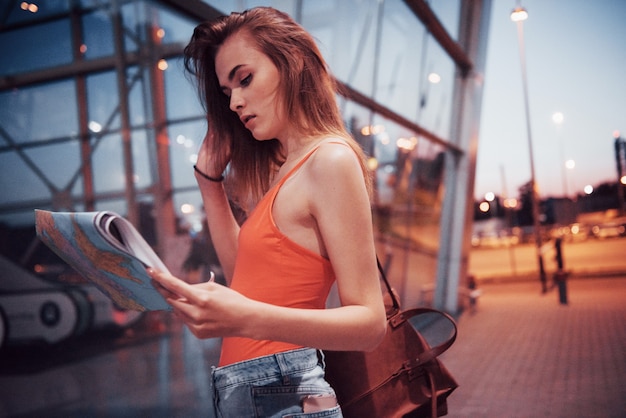 Une belle jeune fille avec un sac à dos derrière ses épaules, debout dans la rue près d'un aéroport. Elle vient d'arriver du reste et très contente!