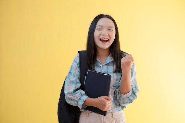 Belle jeune fille avec sac à dos et tenir un ordinateur portable sur fond jaune.