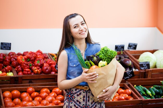 Belle jeune fille avec un sac en papier avec shopping dans un magasin de légumes