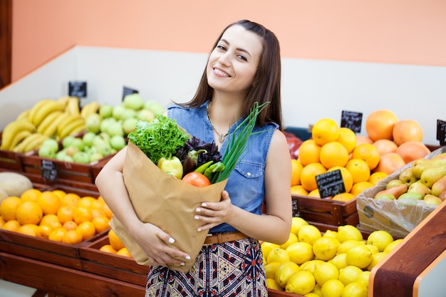 Belle jeune fille avec un sac en papier avec shopping dans un magasin de légumes