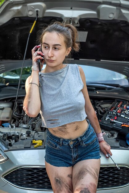 Belle jeune fille sale essayant de réparer sa propre voiture après une panne dans les bois Concept de réparation de voiture Concept de route