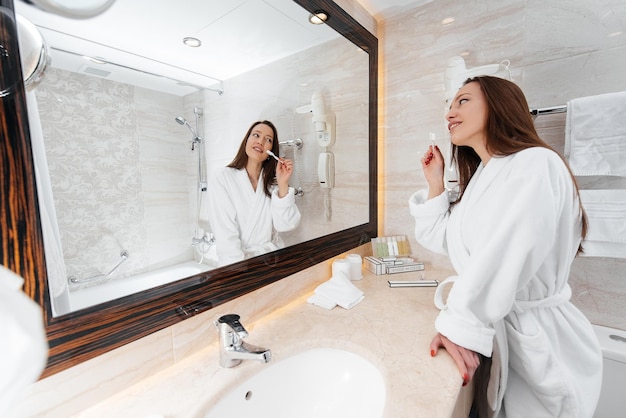 Une belle jeune fille se brosse les dents dans une belle salle de bain blanche Un bonjour frais à l'hôtel Repos et voyage Hôtel loisirs et tourisme