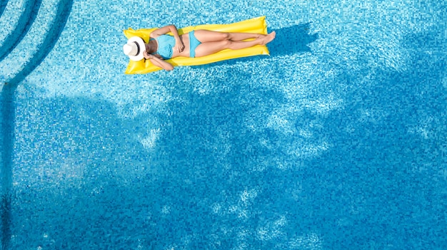 Belle jeune fille se détendre dans la piscine, femme nage sur un matelas gonflable et s'amuse dans l'eau en vacances en famille, station balnéaire tropicale, vue par drone aérien d'en haut