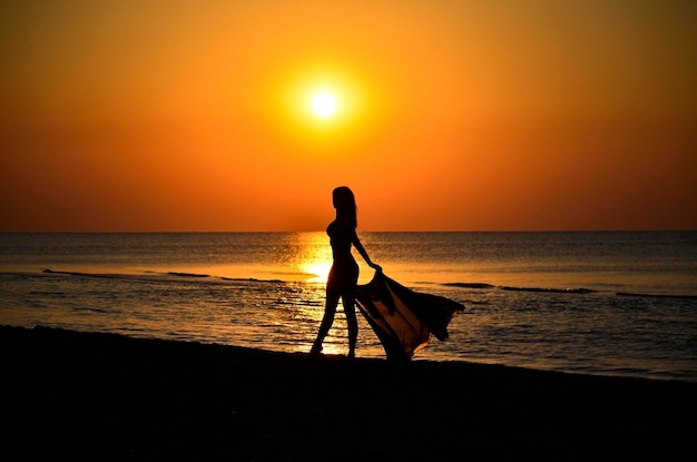 Photo une belle jeune fille se promène le long du rivage de sable le long de l'eau silhouette de dos sombre