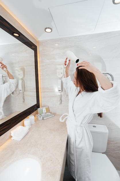 Une belle jeune fille se sèche les cheveux dans une belle salle de bain blanche Un bonjour frais à l'hôtel Repos et voyage Hôtel loisirs et tourisme