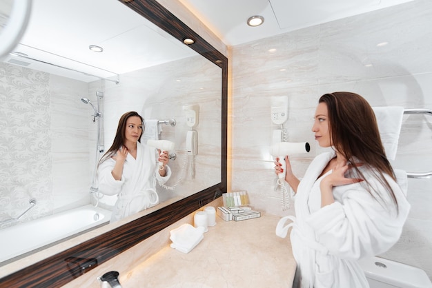 Une belle jeune fille se sèche les cheveux dans une belle salle de bain blanche Un bonjour frais à l'hôtel Repos et voyage Hôtel loisirs et tourisme