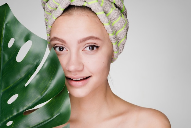 Belle jeune fille avec une serviette sur la tête tenant une feuille verte, profitant du spa et souriant