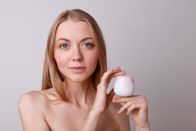 Belle jeune fille soignée avec de la crème dans ses mains sur un mur blanc