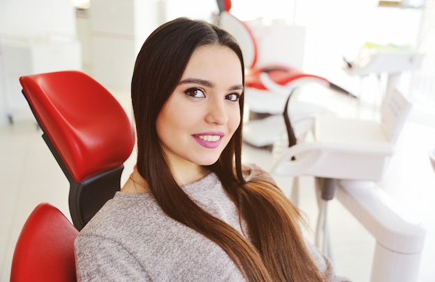 Belle jeune fille souriante dans un fauteuil dentaire rouge