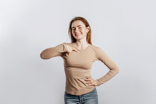 Belle jeune fille souriante et pointant son doigt sur elle-même sur une surface blanche isolée