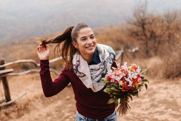 Belle jeune fille souriante avec queue de cheval tenant le bouquet en se tenant debout sur la clairière en automne.