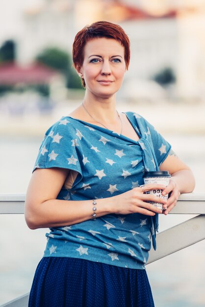 Belle jeune fille souriante rousse aux cheveux courts sur la jetée en chemisier en denim et jupe portrait en plein air.