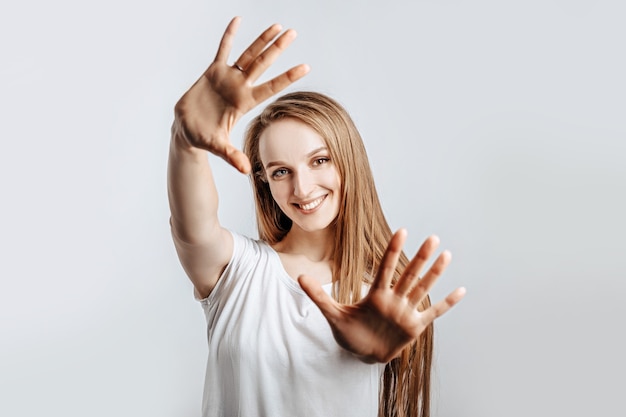 Belle jeune fille souriante et tirant ses mains vers la caméra sur fond gris isolé