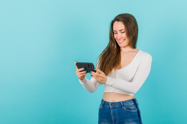 Belle jeune fille sourit en regardant l'écran du smartphone sur fond bleu