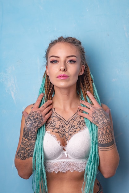 Belle jeune fille avec tatouage et dreadlocks posant dans un soutien-gorge blanc