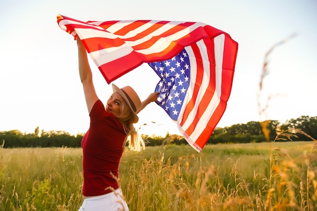 Belle jeune fille tenant un drapeau américain au vent dans un champ de seigle. Paysage d'été contre le ciel bleu. Orientation horizontale.