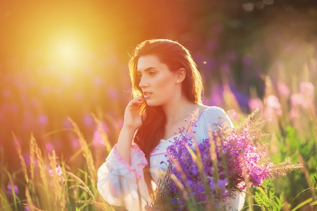 Belle jeune fille, tenant la lavande dans un champ au coucher du soleil.