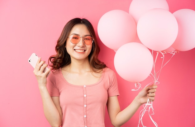 Belle jeune fille tenant un téléphone et un bouquet de ballons joyeux sur un rose