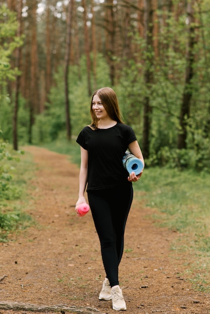 Belle jeune fille en tenue de sport avec une bouteille et un tapis de yoga