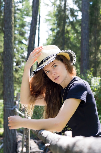 Une belle jeune fille tient un chapeau avec une main sourit dans la nature