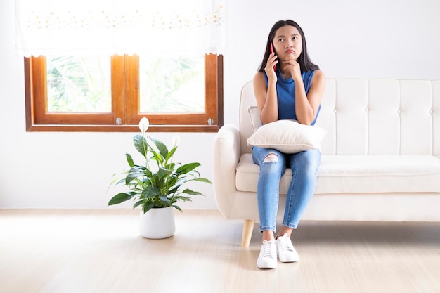 Belle jeune fille utilise un smartphone assis sur un canapé à la maison