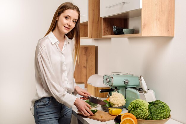 Une belle jeune fille végétarienne ou blogueuse prépare le petit-déjeuner de fruits légumes et légumes verts à la maison dans la cuisine Blog sur une alimentation saine