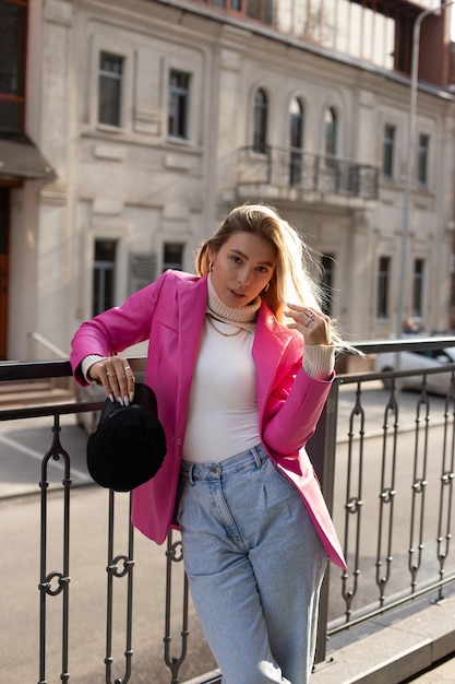 Une belle jeune fille vêtue d'une longue veste rose et d'un chapeau noir marche dans la rue