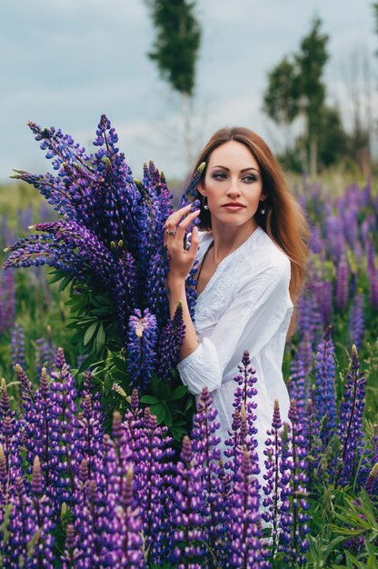 Belle jeune fille vêtue d'une robe blanche debout parmi les lupins