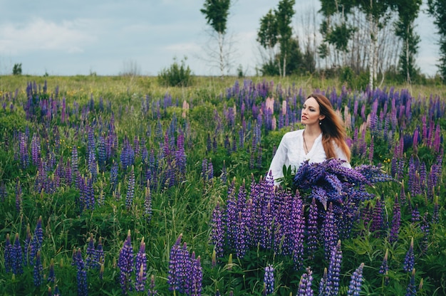 Belle jeune fille vêtue d'une robe blanche debout parmi les lupins