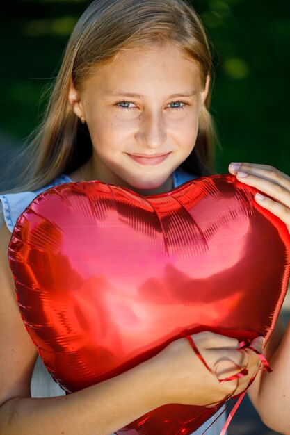 Belle jeune fille vêtue d'une robe bleue avec un ballon en forme de coeur