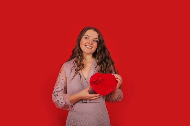 une belle jeune fille vêtue d'une robe rose sur le fond tient une boîte-cadeau de vacances dans ses mains