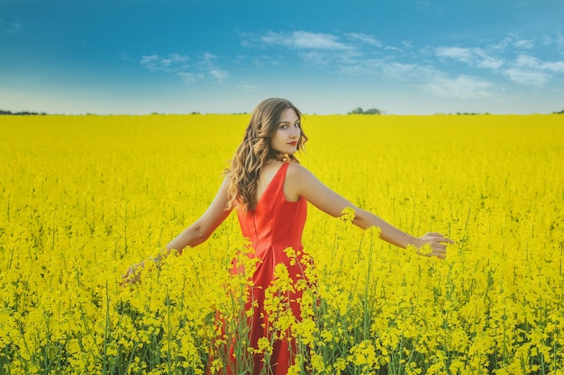 Belle jeune fille vêtue d'une robe rouge se bouchent au milieu du champ jaune avec le gros plan de fleurs de radis.