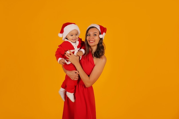 une belle jeune fille vêtue d'une robe rouge tient son fils dans un costume de père Noël et un chapeau de père Noël